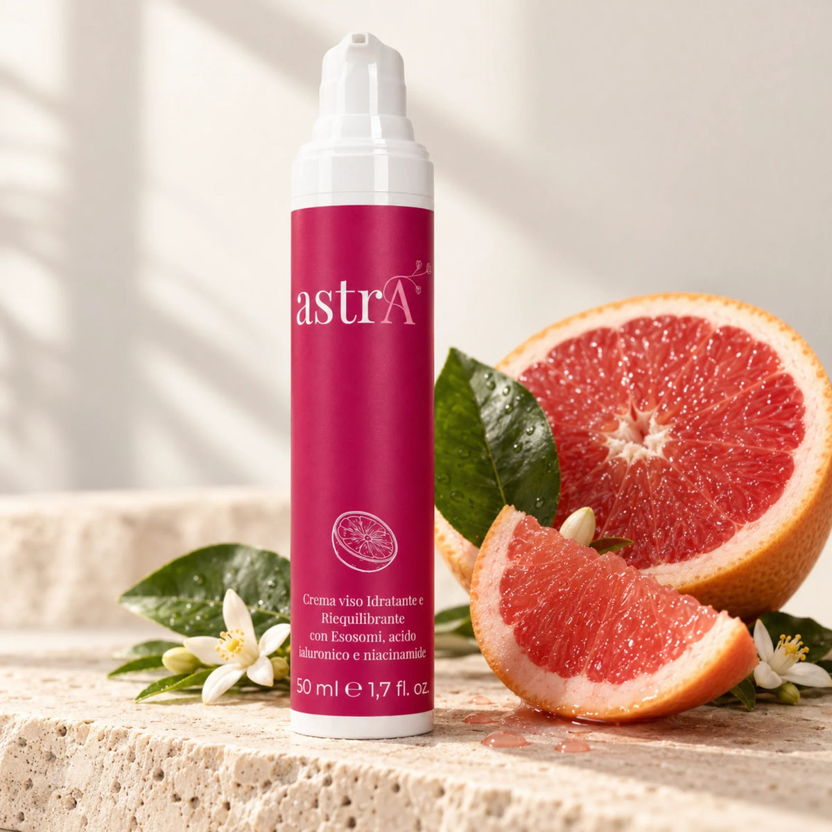 Crema viso astrA su ripiano in travertino accanto a pompelmo rosa