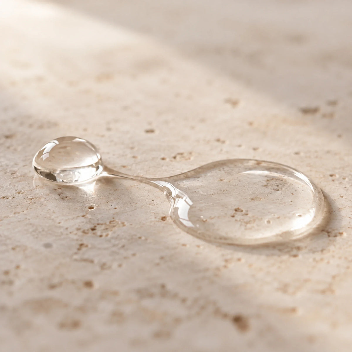 Goccia e scia di texture trasparente del siero viso lyrA su travertino
